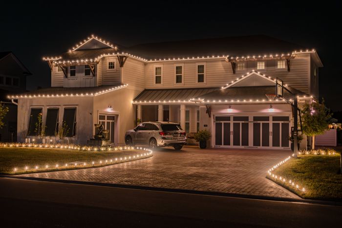 Two-story home lit with warm white lights along every roofline, the driveway and the walkway