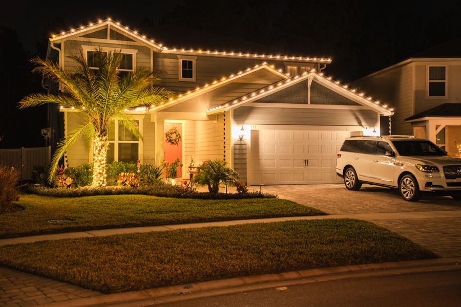 Two-story home with a lit roofline, a wrapped palm and a wreath on the door