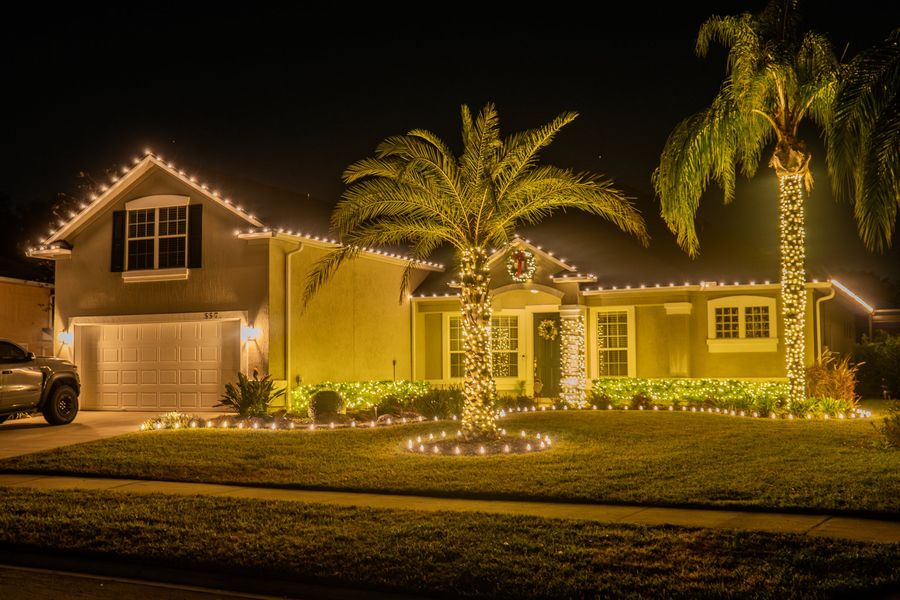 Home with a lit roofline, two palms wrapped in warm white lights and a wreath over the entry