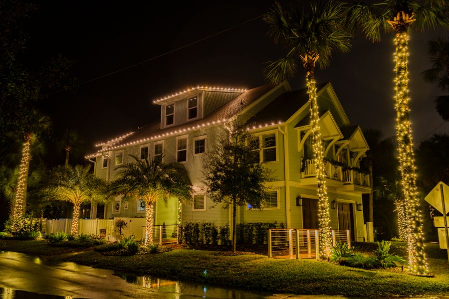 Two-story home with a lit roofline and tall palms wrapped in lights