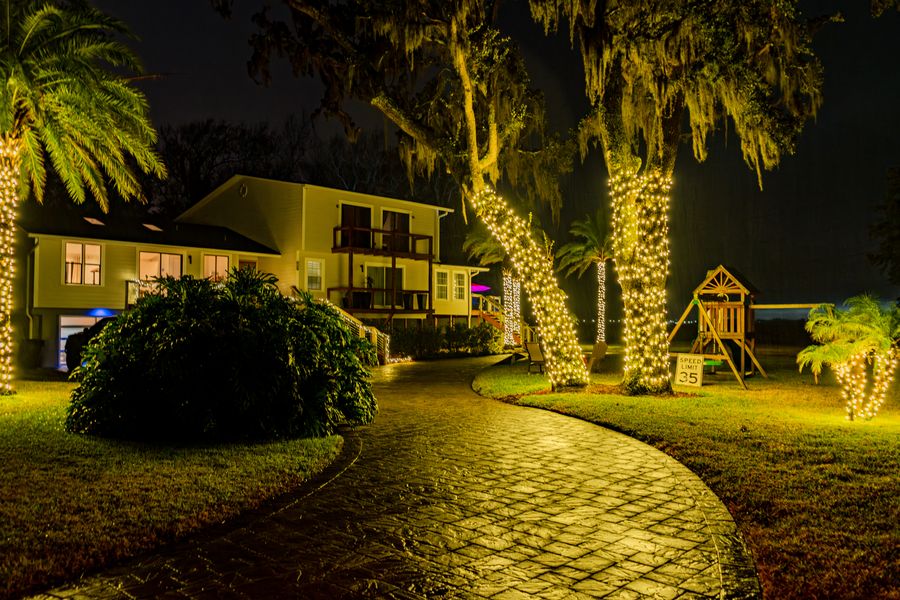 Palm and oak trees wrapped in lights beside a lit paver walkway