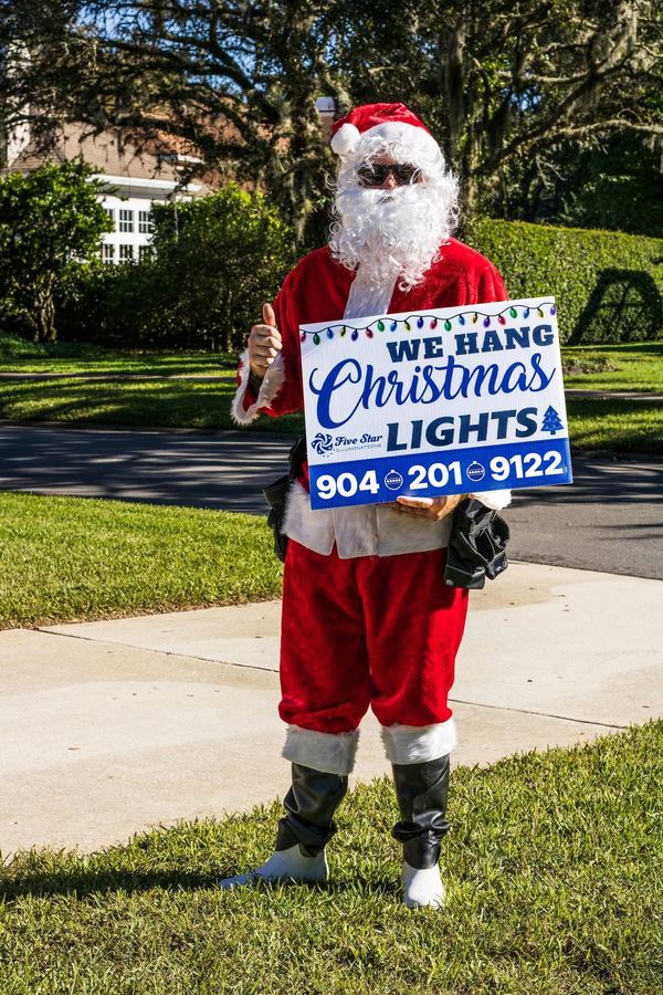 Santa giving a thumbs up and holding a Five Star 'We hang Christmas lights' yard sign